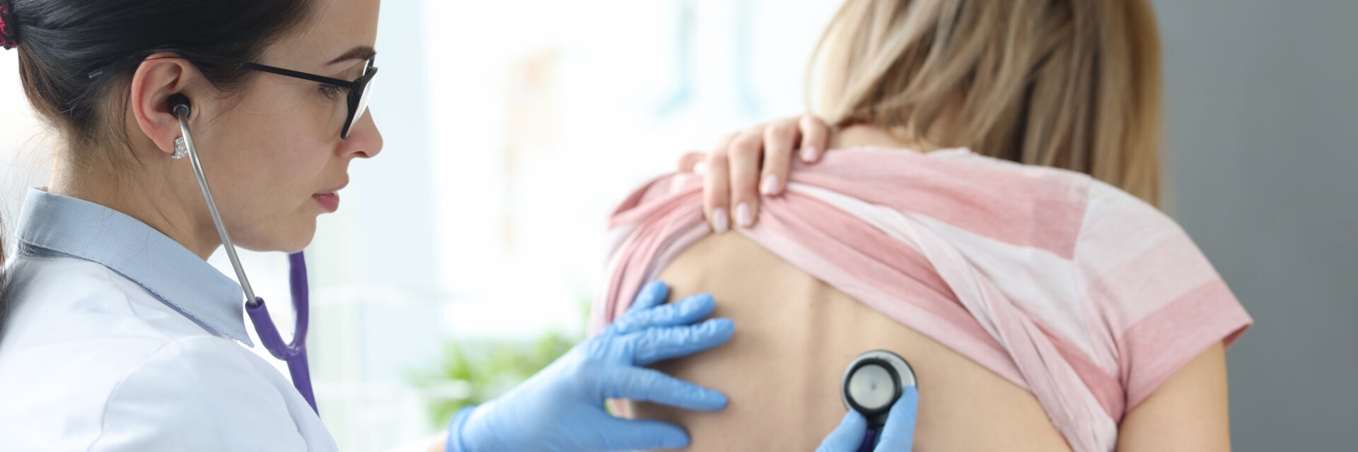 Doctor therapist listening to lungs of patient from back