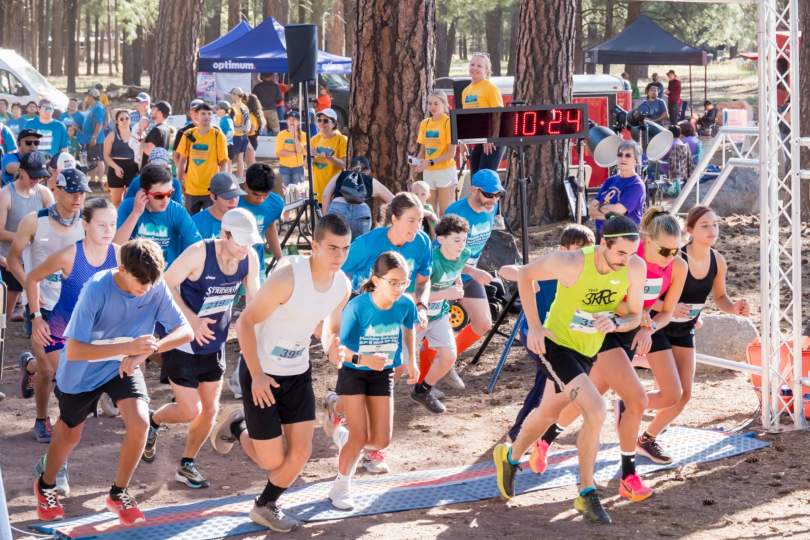 Crowd of runners crossing the start line at a race, with spectators gathered along the course.