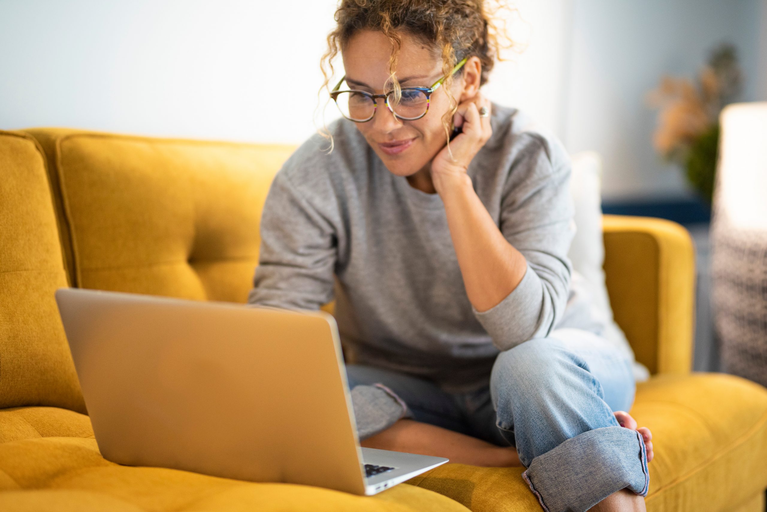 Female sitting on a yellow couch using a laptop and smiling