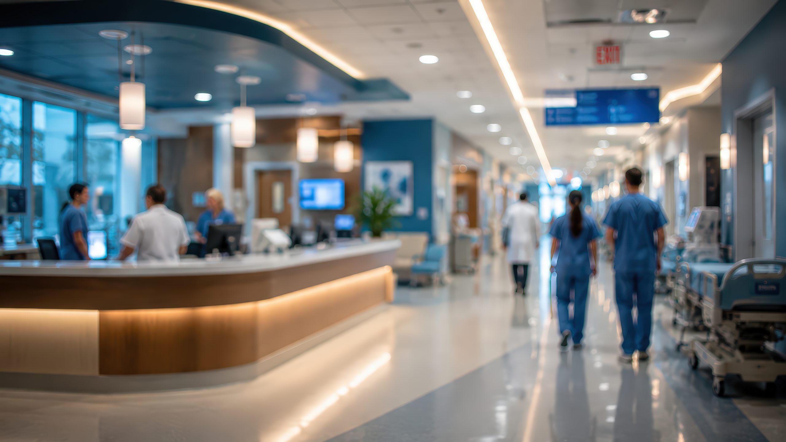 Blurred out view of hospital registration desk with medical providers walking down a hallway