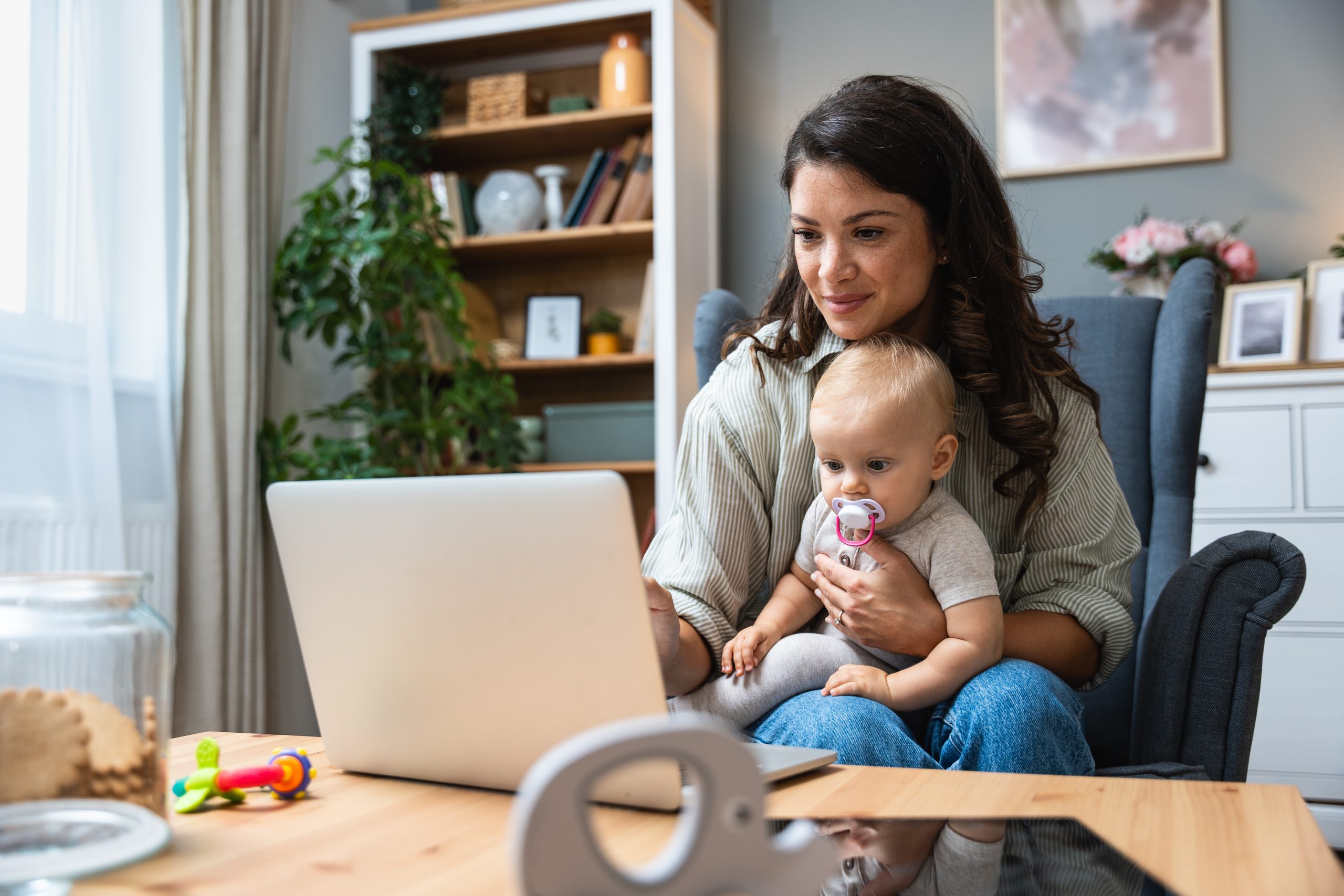 Stay at home mom working remotely on laptop while taking care of her baby.